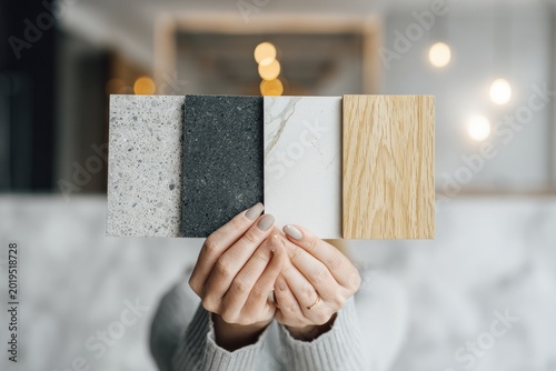 Hands hold four distinct material samples granite, dark stone, marble, and wood