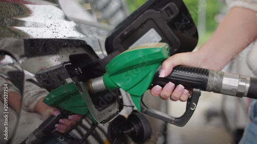Close up of woman hand refueling black car with green fuel nozzle at gas station