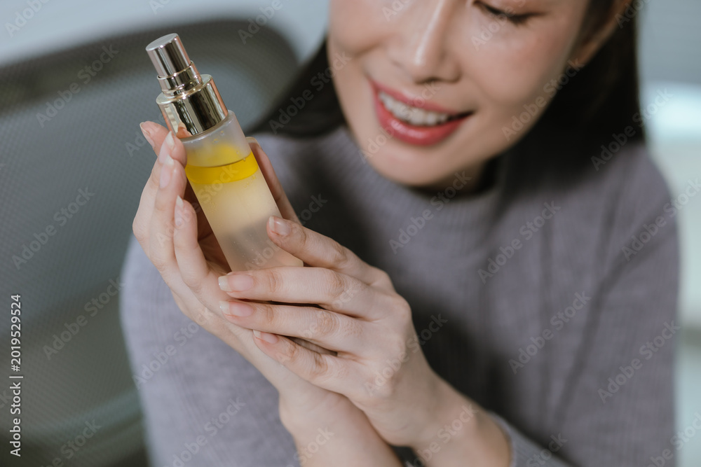 Fototapeta premium Close-up of a smiling young Asian woman holding a hair serum bottle, highlighting beauty, self-care, and healthy hair treatment products.