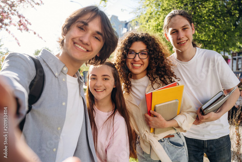 Foto Group of four diverse students smiling for a selfie outdoors, holding books and