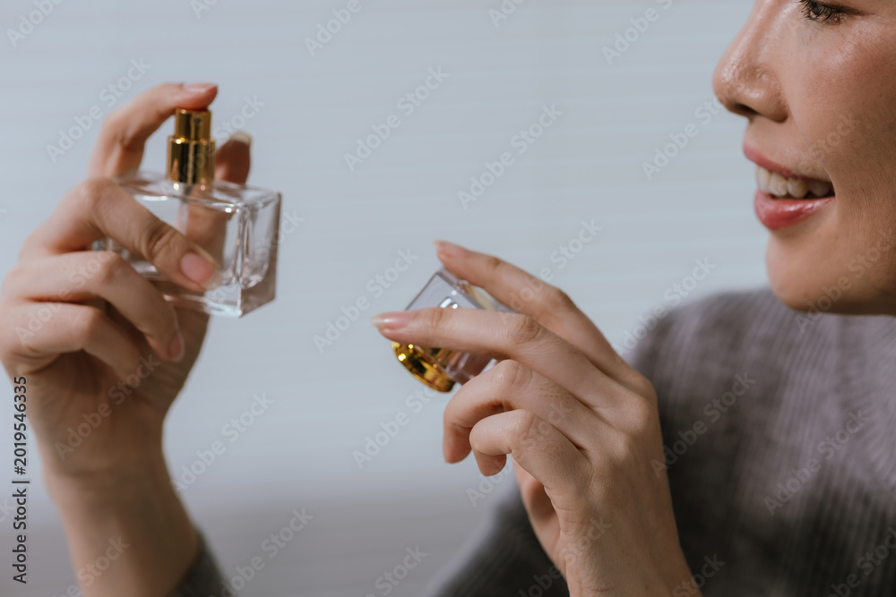 Fototapeta premium Young Asian woman smelling perfume from a luxury fragrance bottle, expressing elegance, beauty, and personal care in a modern lifestyle setting.