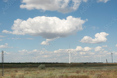 Wind turbine in a field generating clean renewable green energy under a blue sky with clouds.