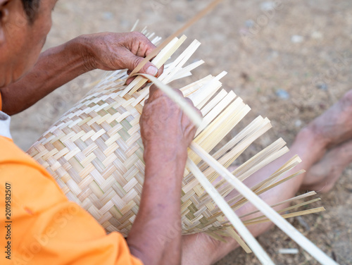 Картината върху платно Close up hands of a man weaving traditional pattern of house, this is Laos local wisdom handcrafted making basketry proceed by an old hand, basket rice cooker and bamboo plate make from bamboo
