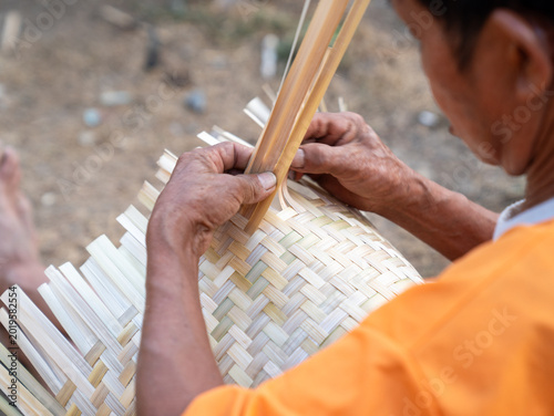Photos Close up hands of a man weaving traditional pattern of house, this is Laos local wisdom handcrafted making basketry proceed by an old hand, basket rice cooker and bamboo plate make from bamboo