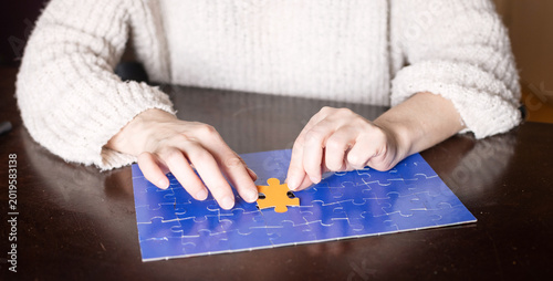 Photography Woman inserting a puzzle piece into a partially completed blue puzzle