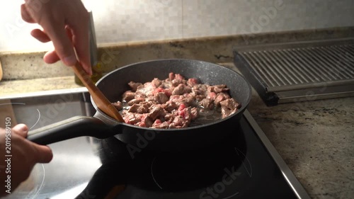 Male hands stirring diced beef with a wooden spatula in a hot non-stick frying pan on a cooktop