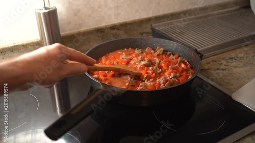 Chef stirring a simmering homemade meat and tomato ragu in a black pan on an induction stove