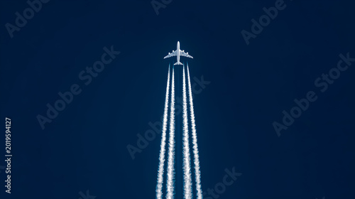 A solitary white commercial airplane ascends through a vast deep blue sky leaving behind a prominent contrail of white vapor that stretches far below creating a striking