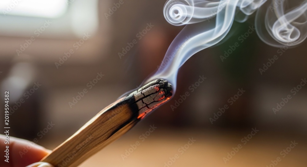 Naklejka premium Closeup of a hand holding burning Palo Santo stick with smoke rising.