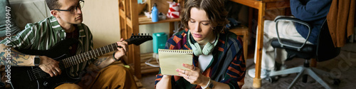 Obraz na płótnie Header of young musicians rehearsing at home, man playing electric guitar, woman writing lyrics in notebook, showing songwriting teamwork