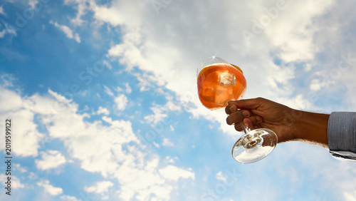 Canvas Print Orange cocktail raised high with dramatic blue sky copy space