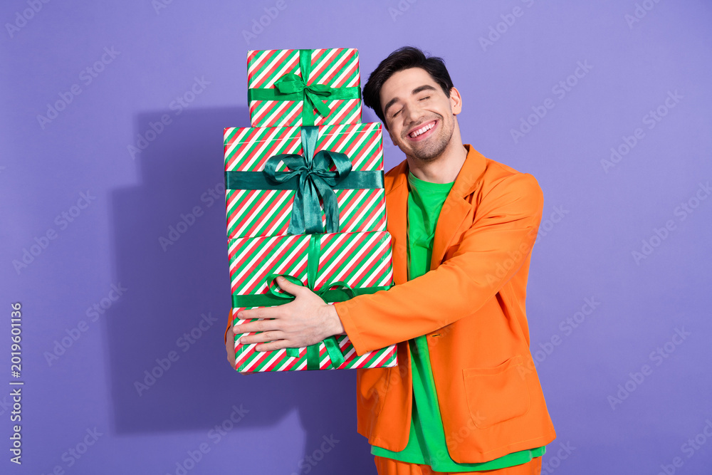 Obraz premium Happy man holding stack of wrapped Christmas gifts in colorful outfit against purple background