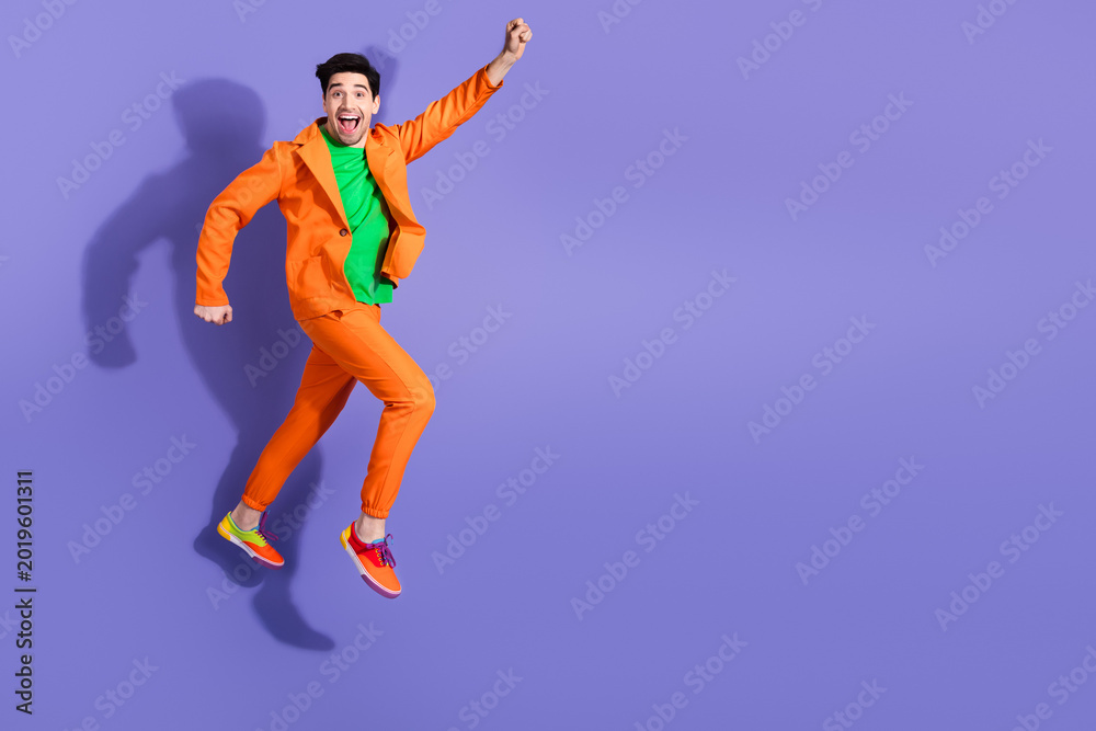 Fototapeta premium Happy man jumping in an orange suit against a purple background celebrating playful colorful fashion and energetic movement for lifestyle and advertising photography