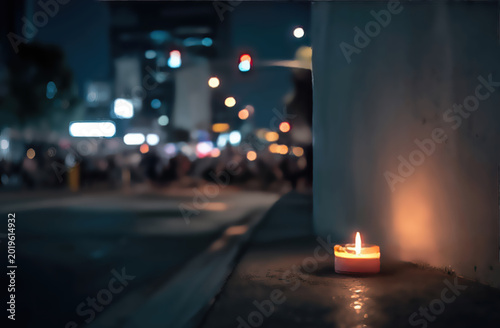 A lone candle flickers on a ledge, illuminating a blurred, bustling city night scene