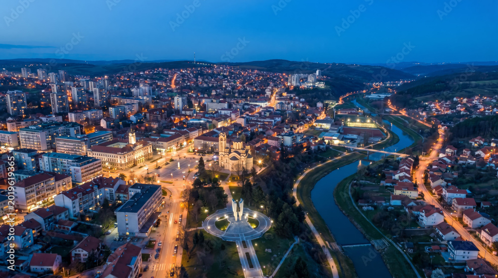 Fototapeta premium Aerial view of a city at dusk with a river winding through it and illuminated buildings.