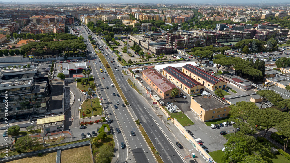 Fototapeta premium Panorama of Via Tuscolana near Cinecittà, in Rome, Italy. Aerial view of a major urban boulevard with multiple traffic lanes, surrounded by commercial buildings, residential districts, and green areas