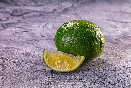 Fotografi Fresh whole lime and a juicy wedge on a textured grey background