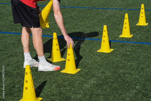 Coach preparing a soccer field for training drill, arranging yellow cones on green turf sports ground