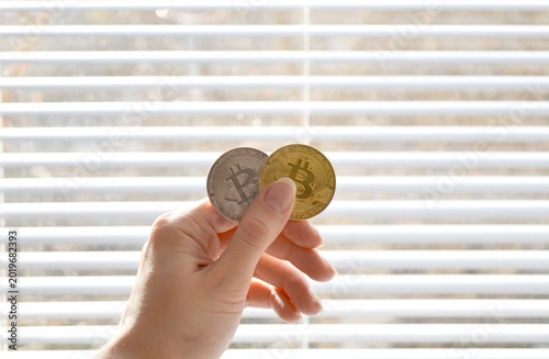 Two Bitcoin coins in a woman's hand in front of a closed window. Cryptocurrency investments, trading, and financial exchange.
