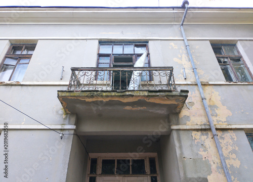 The second-floor balcony is in disrepair. The concrete slab is cracked and crumbling in places, and the railings are broken.