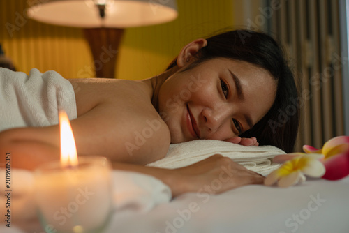 Foto Close up portrait of a happy beautiful young Asian woman smiling and relaxing on a massage bed in a spa salon with a lit candle and plumeria flowers