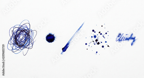 A collection of blue ink splatters scribbles and brush strokes on a white surface