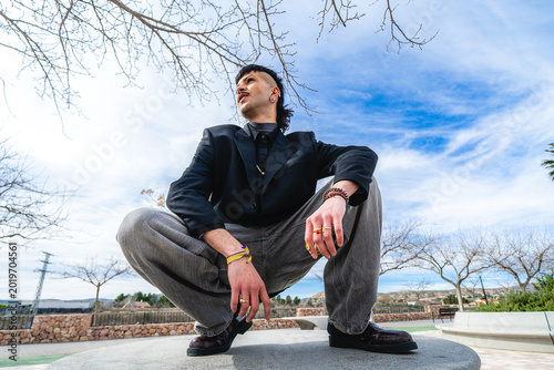 A low-angle shot of a young man crouching down and looking towards the horizon in an outdoor park