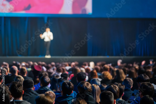 Canvas-taulu Large audience facing blurred presenter on stage during conference, focused atmosphere, professional event, public speaking, live presentation