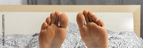 A man is relaxing in bed with his feet sticking out of the covers. He seems to have settled down for the night after a busy day at home or in a hotel room, banner