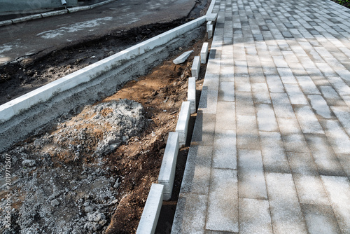 Concrete curb installation progress report. Recent developments in curb and paving alignment. Adjustment of concrete edging alongside new pavement to improve water runoff flow