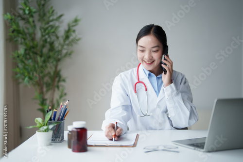 Φωτογραφία Young smiling Asian female physician consulting patient virtually by phone