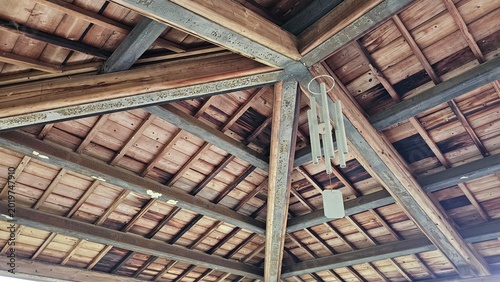 Canvastavla Metal wind chime hanging under wooden pavilion roof, breeze creating crisp sooth
