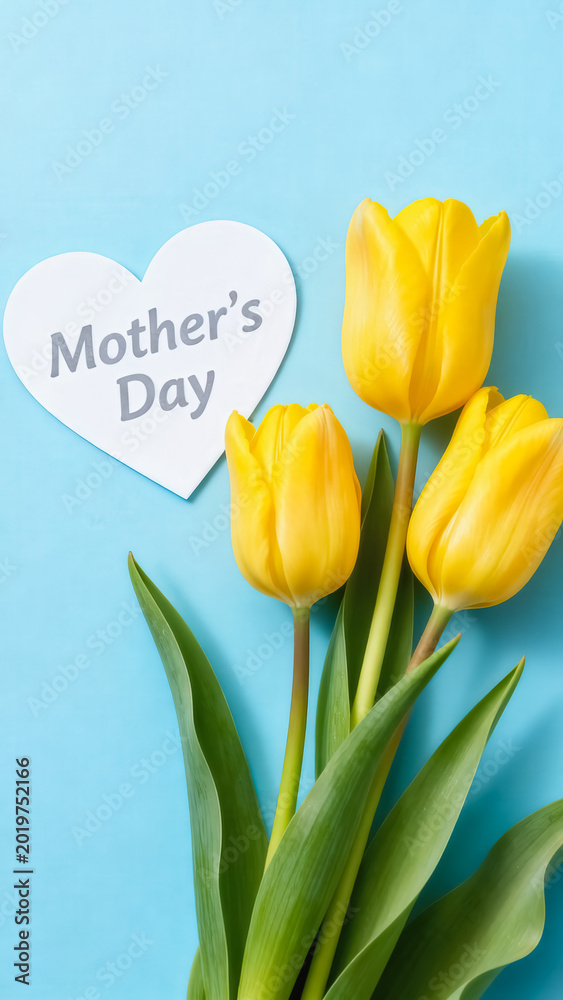Fototapeta premium Flat lay top view of three yellow tulips with a heart-shaped Mother's Day greeting card on a pastel blue background, with copy space.
