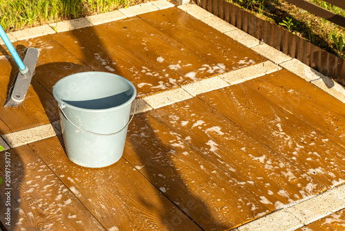 Washing the paving slabs on the terrace in front of the house in the garden, a bucket with hot water and detergent, water with detergent spilled on the tiles to remove dirt from the tiles,