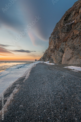 Obraz na płótnie Rocky coastline at sunset with smooth pebbles along the shore, cliffs rising dra