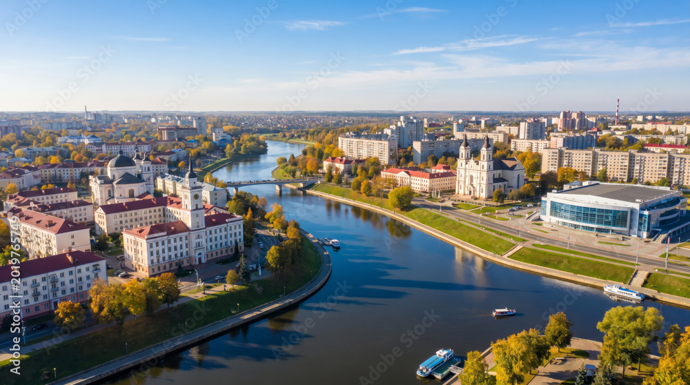 Obraz premium Aerial view of a European city with a wide river flowing through it, featuring modern and historic architecture under a clear blue sky.