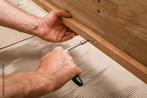 Hands tighten a screwdriver on a wooden furniture panel. Close up of manual assembly and repair work. Home improvement, DIY, and joinery task..