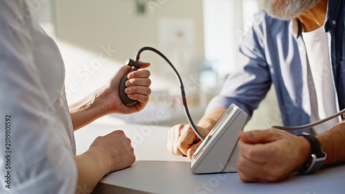 Doctor hands measuring pressure of elderly male patient in pharmacy closeup