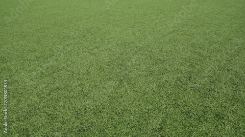 Slow camera movement across a flat artificial football pitch surface. Close view of green synthetic turf with visible texture, highlighting the even field and sports infrastructure under daylight.