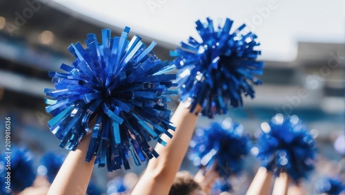 Cheerleaders raising blue pom-poms in a stadium, cheering in sunlight