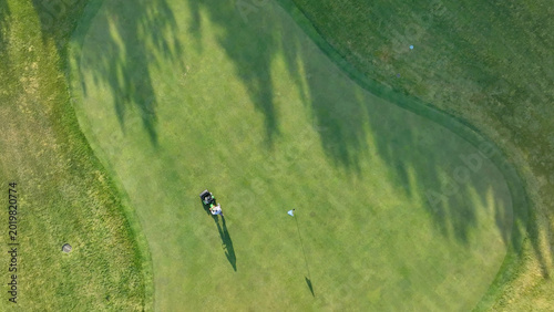 Fotografie Aerial view of a golfer putting on the green with cart and flagstick visible