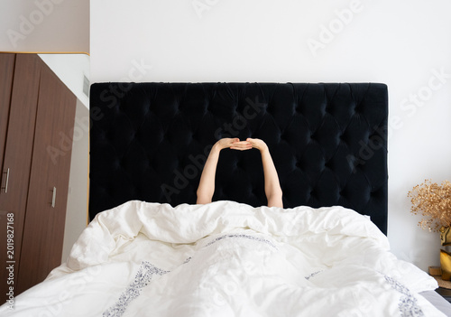 Woman stretching in bed, morning routine, black headboard, white comforter