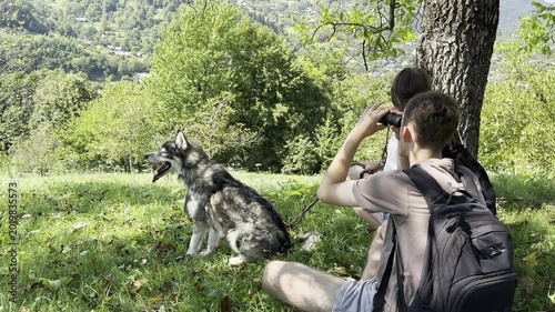 Young hikers with husky dog enjoying nature and exploring landscape with binoculars in forest meadow