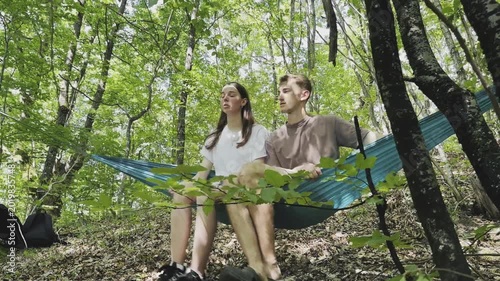 Young people relaxing in a hammock suspended between trees in a green forest