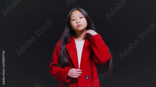 Elegant Asian Girl in Vibrant Red Coat Posing on Black Background with Calm Expression