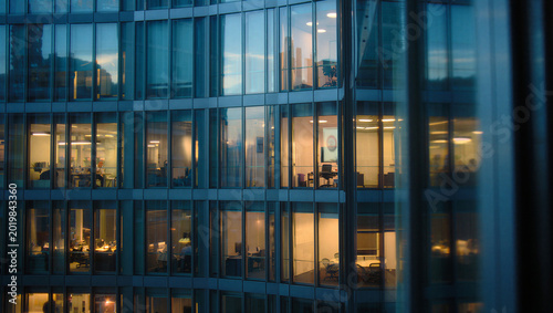 Tableau sur toile Close up view of modern office building glass facade with people working late re