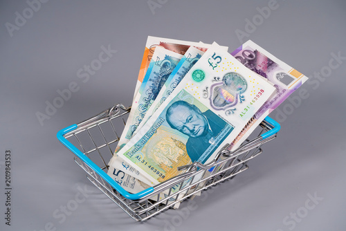 Pound sterling notes in a small shopping basket on a grey background