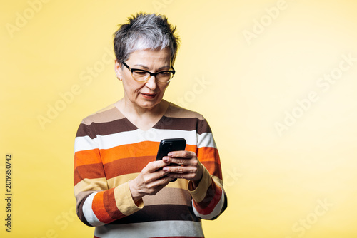 Fotografía Senior woman wearing glasses and striped sweater, actively engaging with her smartphone