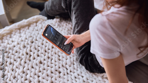 Quadro su tela Woman checking banking app balance on smartphone while sitting on cozy bed
