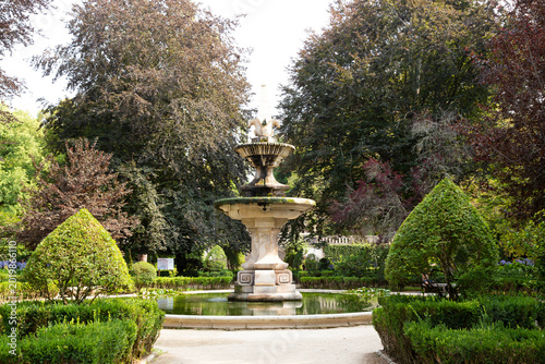Tableau sur toile Ornate Stone Fountain in a Lush Green Formal Garden with Mature Trees